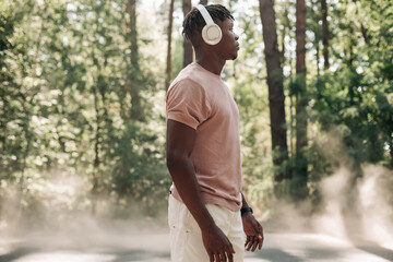 Black sporty man, listening to music on headphones during morning workout, African American man exercising in the park