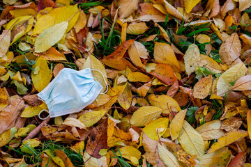 Medical mask lying on the ground, thrown on the ground with yellowed autumn leaves