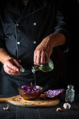 The chef pours olive oil into a fresh red cabbage salad. Cooking healthy food in restaurant kitchen on vintage table.