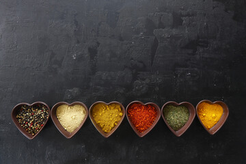 Different kind of spices on a black stone. Oriental spices in in heart shaped bowl, red peppers,...