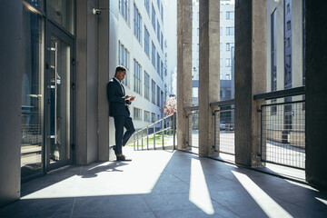 Male businessman near office reads news from tablet computer, african american freelancer in...