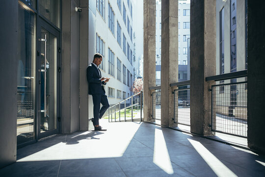 Male businessman near office reads news from tablet computer, african american freelancer in business suit near office outside