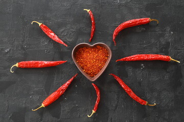 red hot chili peppers powder in heart shaped bowl on black stone table. Love concept. Top view flat lay with copy space