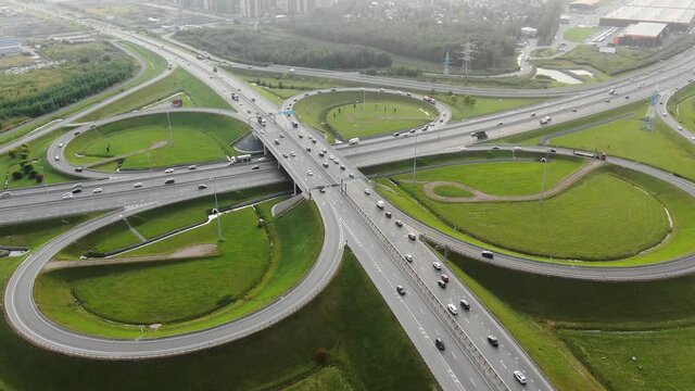 Huge autobahn multilevel traffic intersection with driving cars among green meadows near entrance of city aerial panorama