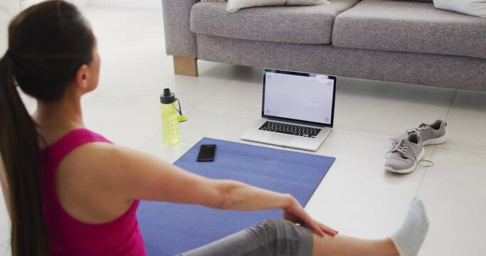 Back view of asian woman on mat exercising with laptop with copy space on screen at home