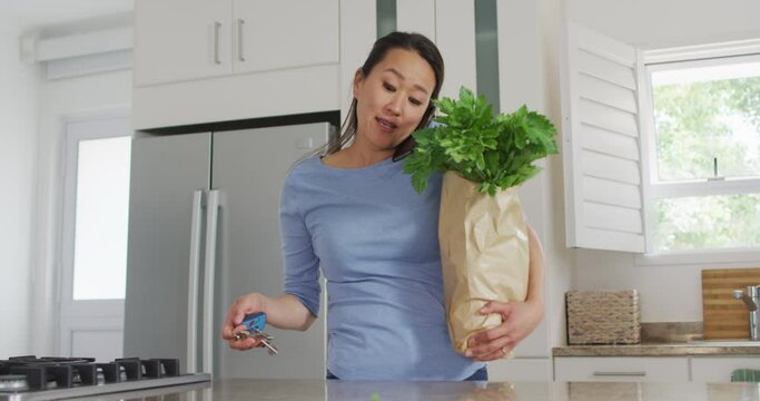 Asian woman coming back home with groceries and having call on smartphone