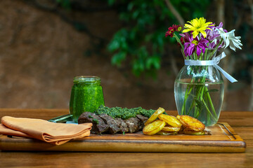 Meat with pesto and french fries. Vase of beautiful flowers.