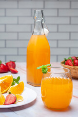 fruit juice and natural orange in glass and bottle with fresh oranges and strawberries on marble counter and white wall