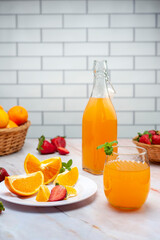 fruit juice and natural orange in glass and bottle with fresh oranges and strawberries on marble counter and white wall