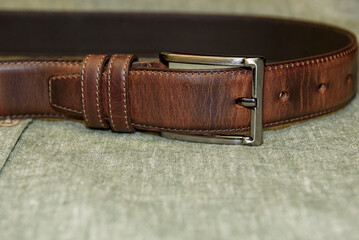 A brown men's leather belt lies on a green cotton shirt.