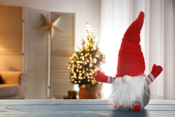 Funny Christmas gnome on blue wooden table in room with festive decorations. Space for text