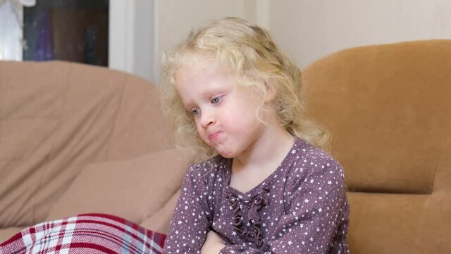 a cute girl with curly blond hair was offended and puffed out her cheeks, a disgruntled Caucasian girl on a chair