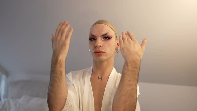 Extravagant LGBT woman opening eyes with beautiful makeup and false eyelashes shaking hands looking at camera. Medium shot portrait of confident proud Caucasian gender-fluid person posing indoors