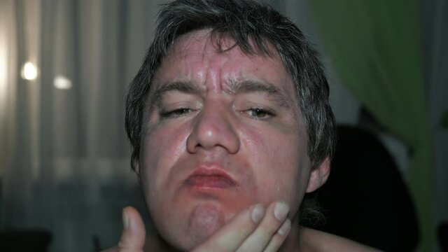 an adult man with a bare torso rubs a red, fat, irritated and sweaty face after shaving in close-up in front of a mirror with a jumping focus.
