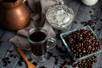 coffee in fresh beans with cup of coffee and old coffee pot with dark wooden background and dark style sugar bowl
