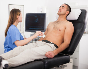 Obraz premium Young woman doctor and patient during the ultrasound examination of abdomen in medical office