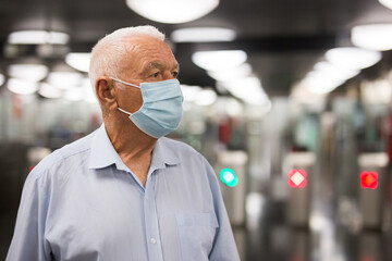 Fototapeta na wymiar European old man in face mask standing beside turnstile in subway station.