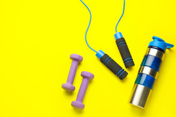 Dumbbells, skipping rope and bottle of water on yellow background