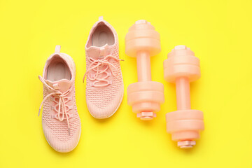 Dumbbells and shoes on yellow background