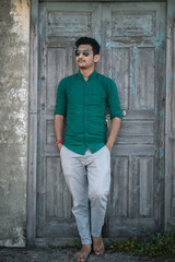 Male model standing and looking sideways wearing green shirt, sunglasses. Standing outdoor in...