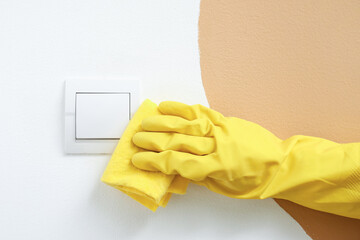 Woman wiping switch on color wall, closeup