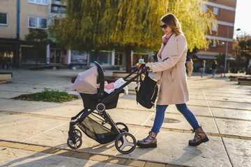Side view full length of caucasian woman mother pushing stroller with baby in the city in autumn...