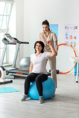 Mature woman training with fitball and physiotherapist in rehabilitation center