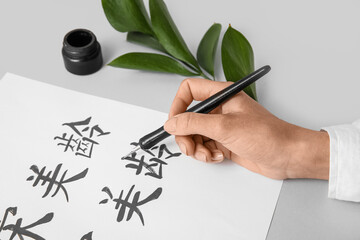 Asian calligraphist writing hieroglyphs on light background