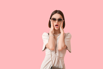 Shocked woman in stylish sunglasses and jewelry on color background