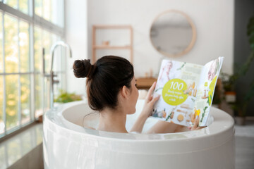 Pretty young woman reading magazine while taking bath at home