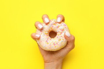 Woman with beautiful manicure holding delicious doughnut on yellow background