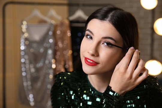 Beautiful young woman applying mascara in dressing room at night, closeup