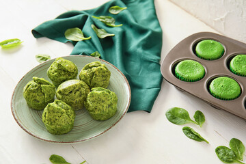 Plate and baking tin with tasty spinach muffins on table