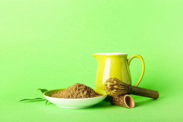 Saucer with hojicha powder, jug of milk and chasen on green background