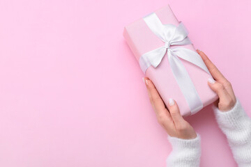 Woman holding gift box on pink background, closeup