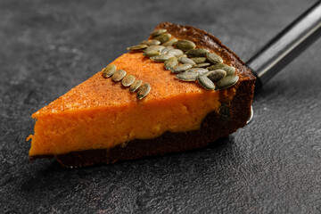 Spatula with piece of delicious pumpkin pie on black background, closeup