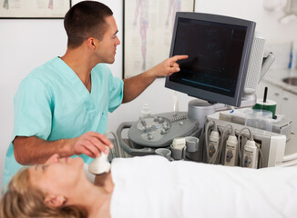 young doctor conducting ultrasound examination of patient's thyroid lying in clinic