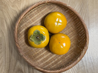hard persimmons in a bamboo basket on wooden table
