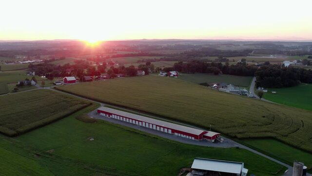 Descending aerial on storage facility in rural farm countryside at summer sunrise, sunset.