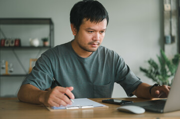 Asian business man thinking while serious working on laptop sitting on desk in modern office at home ,co-working space or at home with copy space, webinar over the internet.