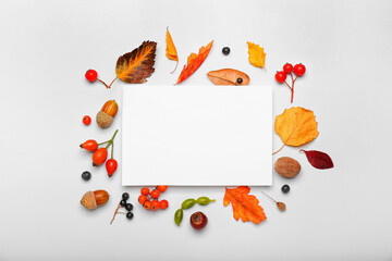 Fototapeta premium Autumn harvest frame with blank white card, seasonal fall leaves, berries, and nuts on a light background