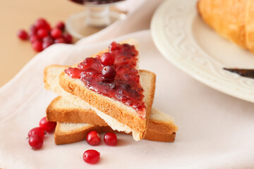 Tasty toasts with lingonberry jam and fresh berries on beige wooden background