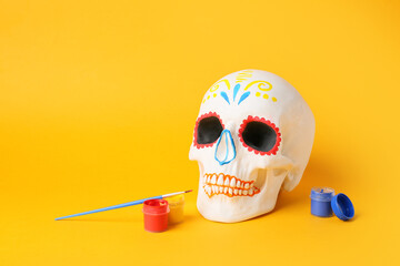 Human skull for Mexico's Day of the Dead (El Dia de Muertos) with brush and paints on yellow...