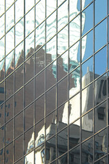 Fototapeta na wymiar Glass tower office building exterior windows reflecting and distorting nearby skyscrapers and blue sky in Midtown Manhattan, New York City 