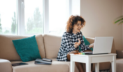 Woman sitting on sofa in front of computer communicating with people in an online conference. Quarantine lifestyle
