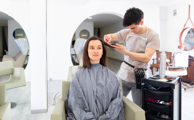 Young positive guy professional hairdresser cut woman's hair in hairdressing salon