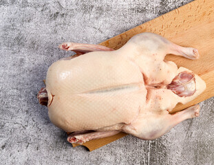 Whole raw duck on a rectangular cutting wooden board on a dark grey background. Top view, flat lay