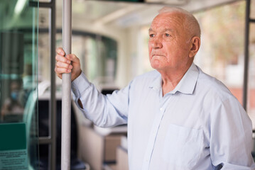 Fototapeta na wymiar Senior European man standing inside tram and waiting for his stop.