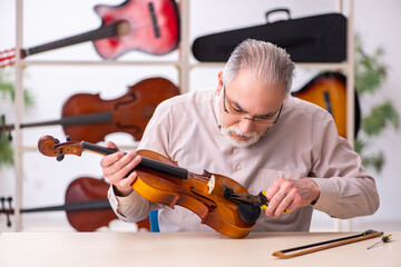 Old male repairman repairing musical instruments at workplace