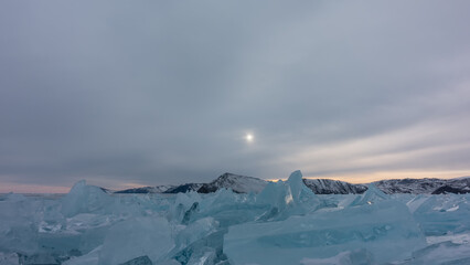 Blocks of turquoise hummocks on a frozen lake. The glare of the sun on the edges. A mountain range...